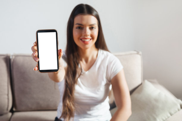 白天，明亮的房间里，一位女士坐在沙发上，手中拿着一部屏幕空白的智能手机图片下载