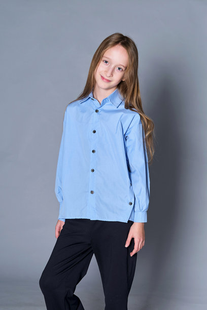 身穿浅蓝色衬衫和黑色裤子的小女孩，微微侧着头，脸上带着温柔的笑容。这张照片捕捉了童年的纯真与温暖，突显了她友善的性情。图片下载