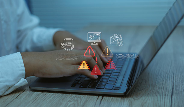 一名商人正在使用笔记本电脑打字，屏幕上显示数字警报图标、安全符号，概念涉及网络安全风险、系统错误、数据邮件保护、恶意软件检测和信息技术安全。图片下载
