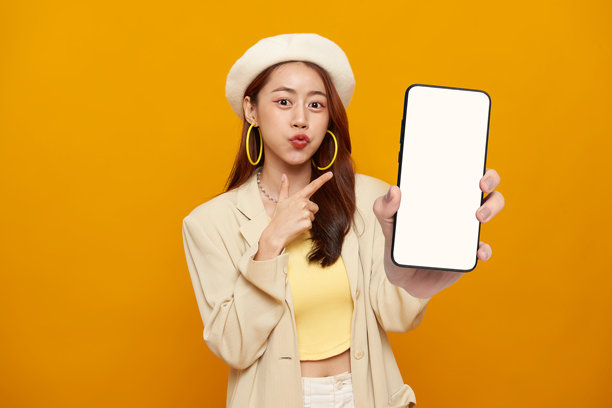 时尚生活推广肖像，一位微笑的亚洲女性手持带有空白屏幕的智能手机模型，在黄色工作室背景下展示现代数字营销移动应用。图片下载