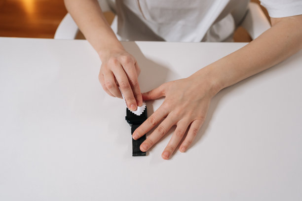 俯视视角，年轻女性正在擦拭智能手表屏幕，准备贴上保护膜。清洁表面以防刮擦和损坏。图片下载