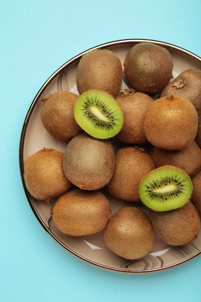 绿色的猕猴桃放在盘子里，背景是蓝色。热带水果。竖直照片。图片下载