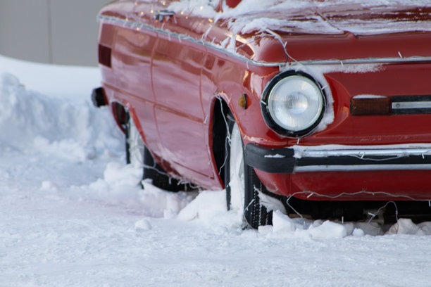雪中红色复古汽车的侧面特写，车上挂着节日彩灯图片下载