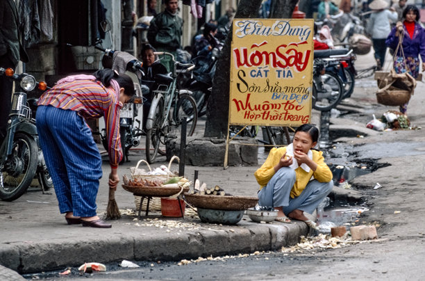 越南河内“三十六行街”街边，一位女孩蹲着吃零食的历史彩色照片，摄于1995年3月5日图片下载
