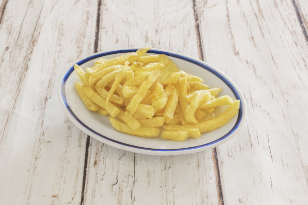 一张自然光下的照片，展示了刚沥干油的炸薯条在质朴的陶盘上，散发出淡淡的光泽图片下载
