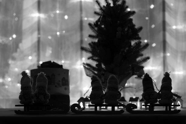 圣诞树和发光装饰的背景下的玩具天使和雪橇。黑白照片。图片下载