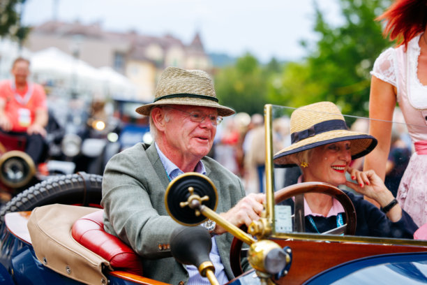 一对年迈夫妇在老爷车节上享受复古汽车之旅，展示了经典汽车、节日气氛和充满活力的周边环境图片下载