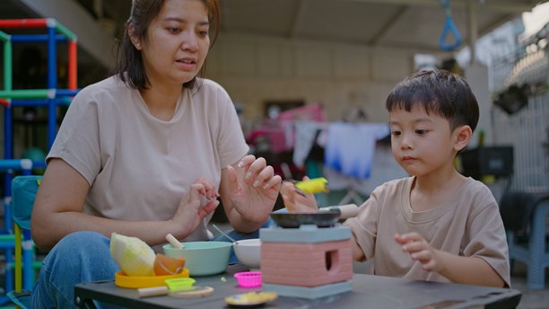 男孩和妈妈在花园里玩耍微型厨房玩具的抓拍照片图片下载