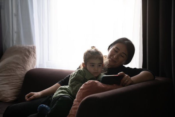 妈妈和她的小女儿坐在沙发上看手机视频的抓拍照片图片下载