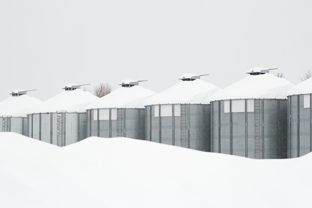 降雪后覆盖着积雪的钢制粮仓的单色照片。图片下载