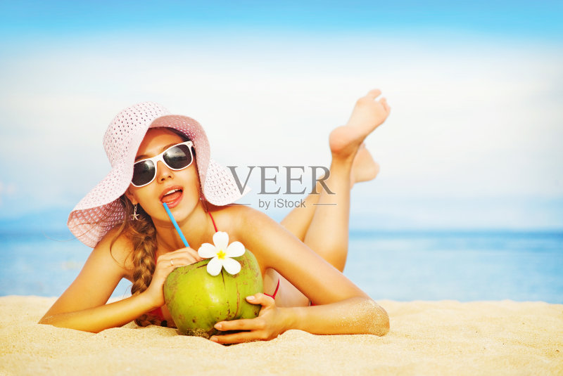 年轻女子穿着粉红色泳衣，喝着椰子鸡尾酒正版图片素材