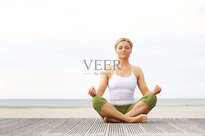 美丽的年轻女子坐在瑜伽莲花姿势在海滩正版图片素材