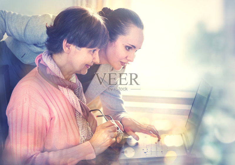 帮助一位老人使用笔记本电脑上网搜索的妇女正版图片素材