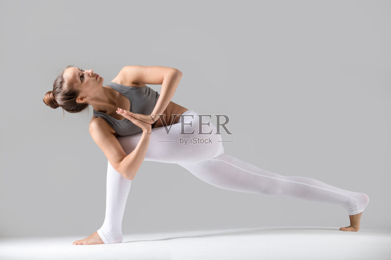 年轻女子在Parivrtta Parsvakonasana姿势与合十礼，灰色正版图片素材