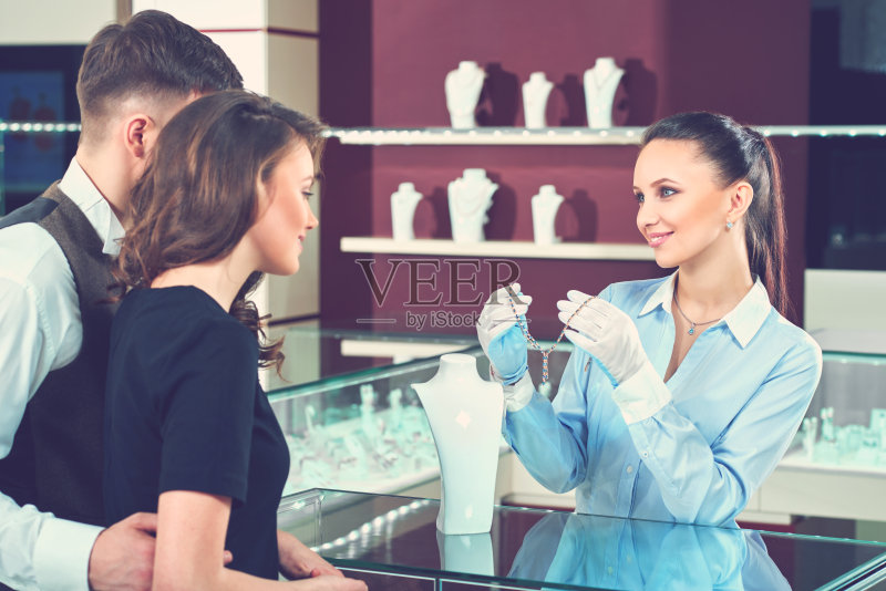 在珠宝店微笑的卖家向买家展示项链。正版图片素材