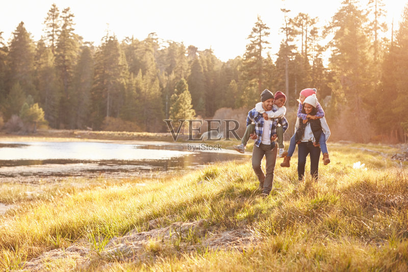 父母让孩子骑在背上在湖边散步正版图片素材
