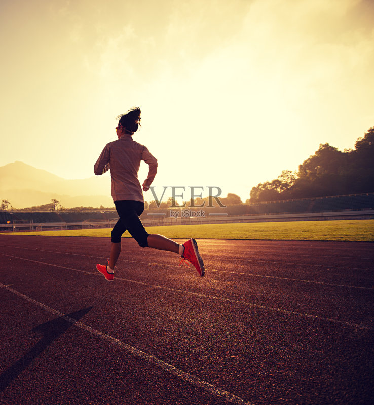 年轻女子在阳光明媚的早晨在体育场跑道上跑步正版图片素材