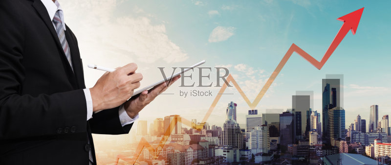 商人工作的数字平板电脑，全景城市和上升的箭头正版图片素材