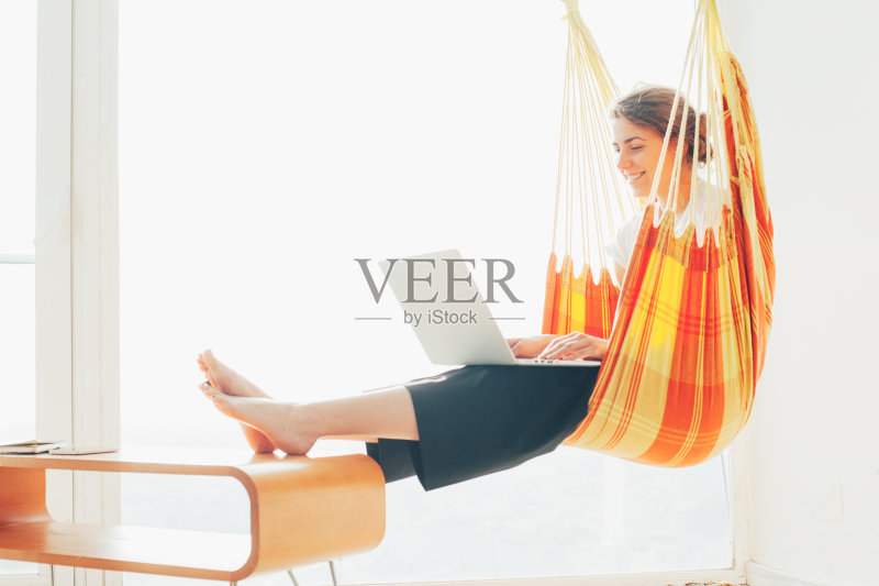 在吊床上拿着笔记本电脑的女人正版图片素材