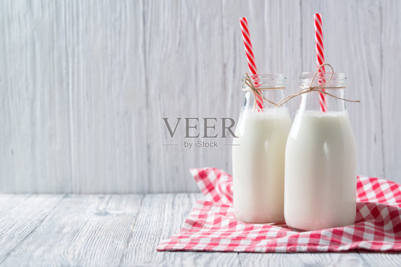 木制背景上有红色吸管和格子毛巾的牛奶瓶正版图片素材