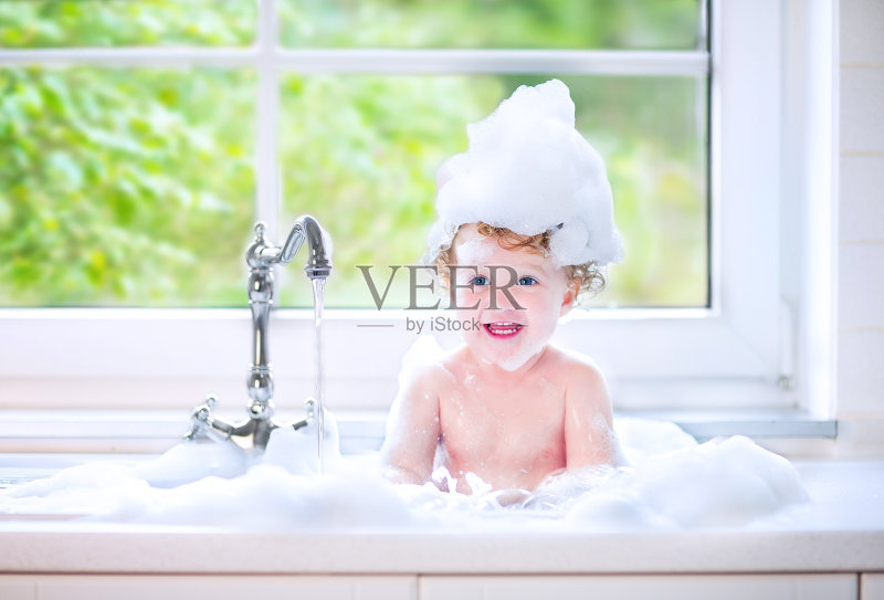 笑着的小女孩在厨房的水槽里满是水和泡沫正版图片素材