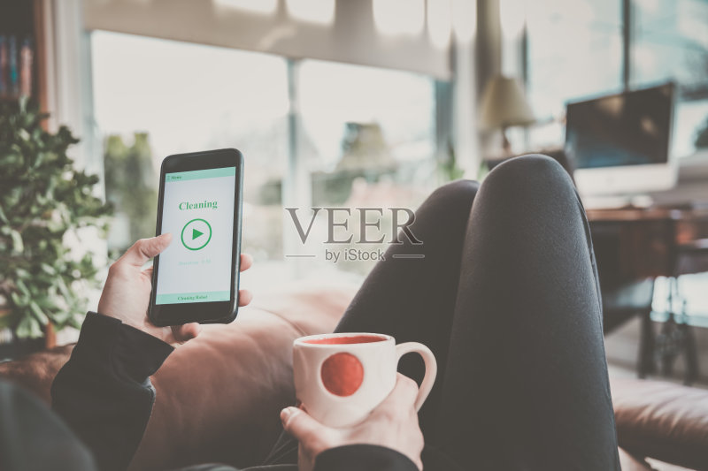 一名女性在手机上使用家庭机器人清洁应用程序正版图片素材