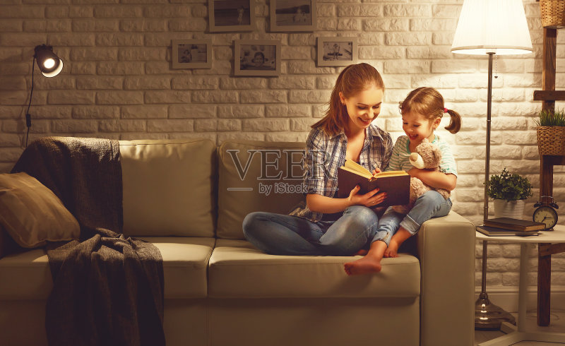 晚上睡觉前，妈妈会在台灯旁给女儿读书正版图片素材