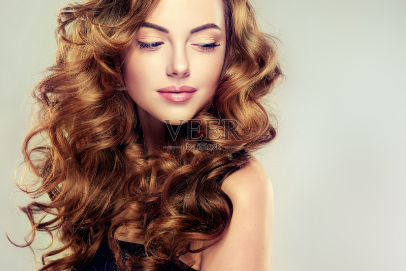 年轻的，棕色头发的女人，有着卷卷的，有光泽的卷发。正版图片素材