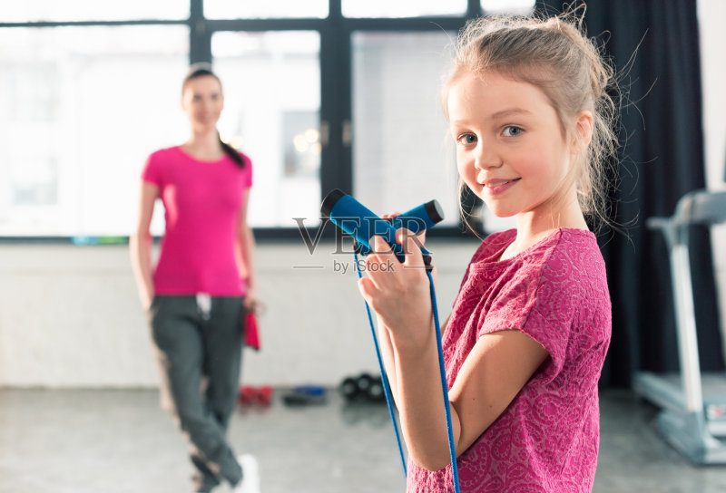 妈妈看着可爱的小女儿拿着跳绳，对着镜头微笑正版图片素材