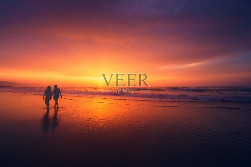 日落时分，一对情侣在海滩上散步正版图片素材