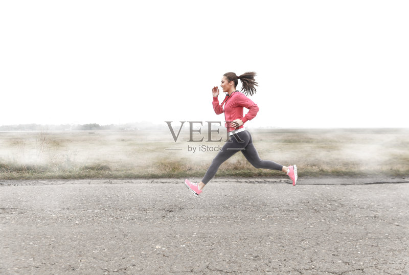 一个年轻的健身妇女在一个有雾的早晨在一条开阔的道路上跑步。正版图片素材