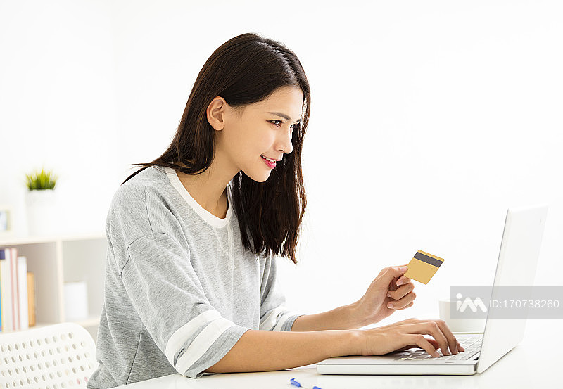 手持信用卡并看着笔记本电脑的年轻女人照片摄影图片