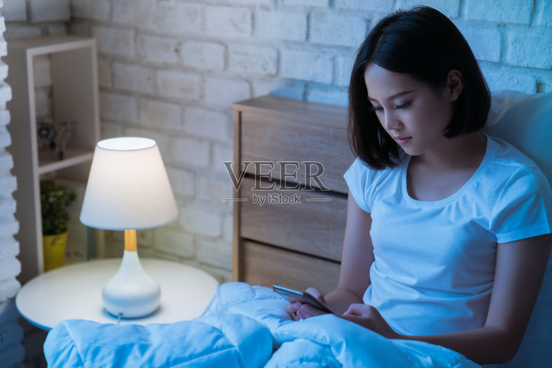 亚洲女性晚上睡觉前会在床上使用智能手机。手机成瘾的概念。正版图片素材