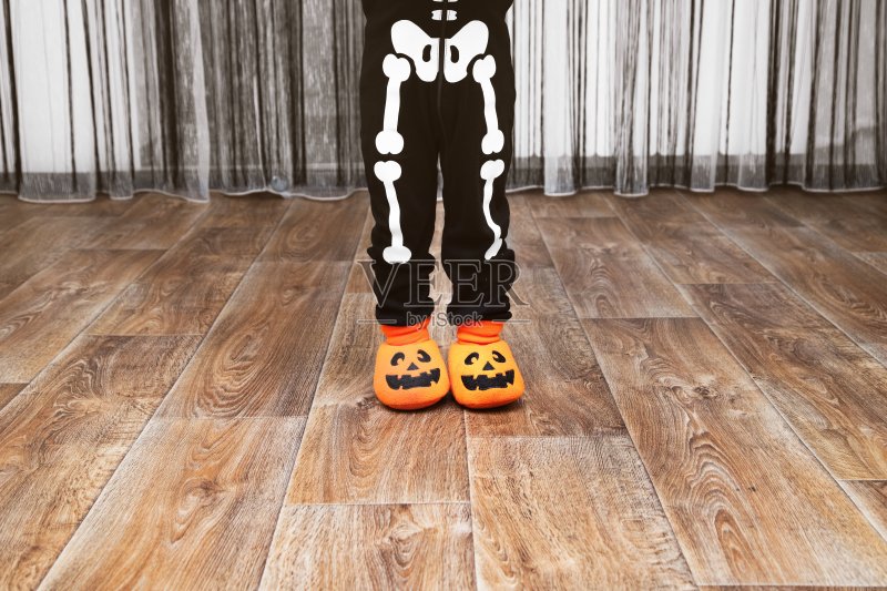 穿着骷髅装和南瓜拖鞋的小男孩站在房间中央正版图片素材
