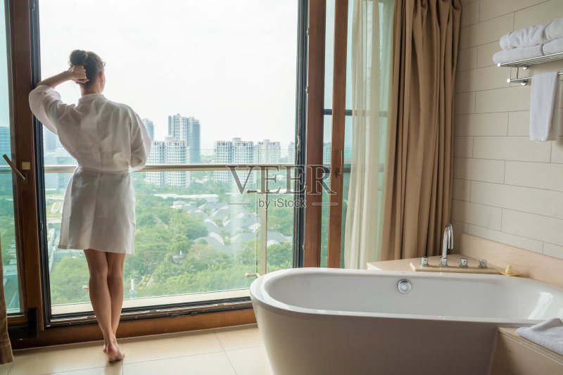年轻女子在豪华浴室白色浴衣与城市景观正版图片素材