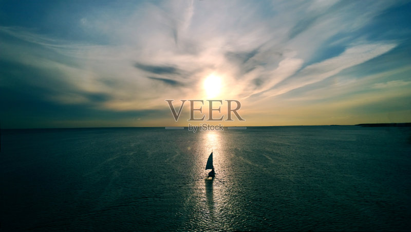 一艘白色的小船在夕阳的余晖中漂向地平线。美丽的云彩与黄色的亮点。鸟瞰图正版图片素材