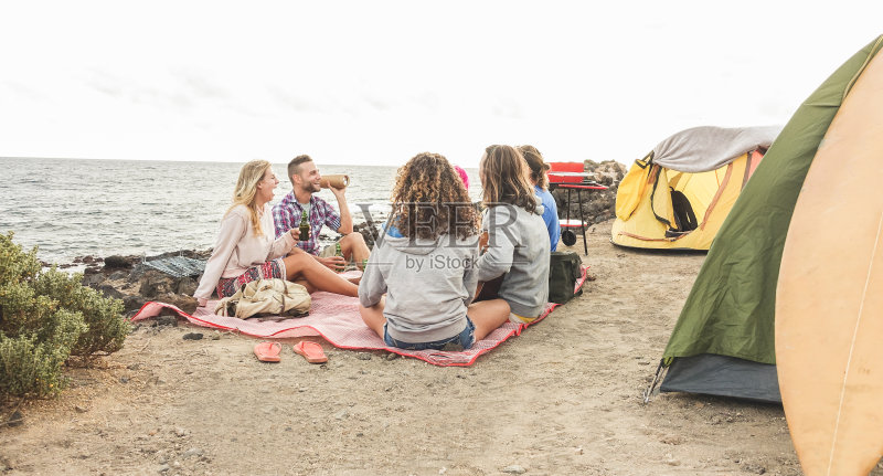 快乐的朋友烧烤野餐旁边的海洋-时髦的人玩音乐，露营和一起欢笑的假期-旅游，假期，派对和友谊的概念正版图片素材