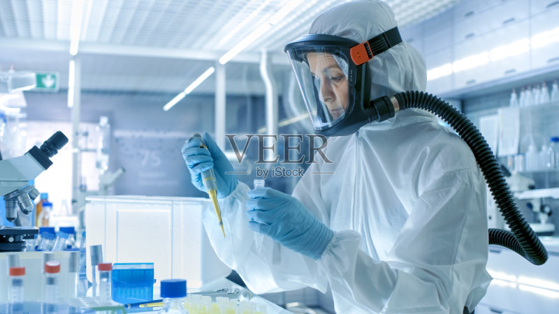 医学病毒学研究科学家工作在防护服与面具，她使用微型吸管。她在一个无菌的高科技实验室工作，研究设施。正版图片素材