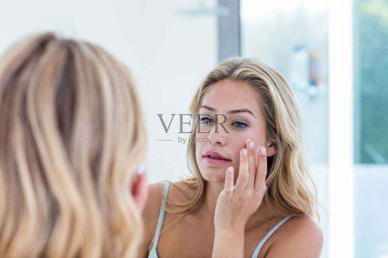 微笑的漂亮女人在她的脸上涂抹奶油正版图片素材