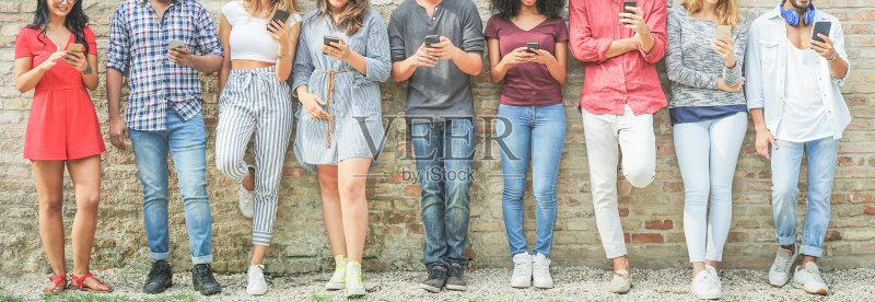 不同文化背景的人们在户外使用手机——朋友们享受科技潮流的乐趣——青年、新一代的沉迷与友谊概念——暖色滤镜正版图片素材