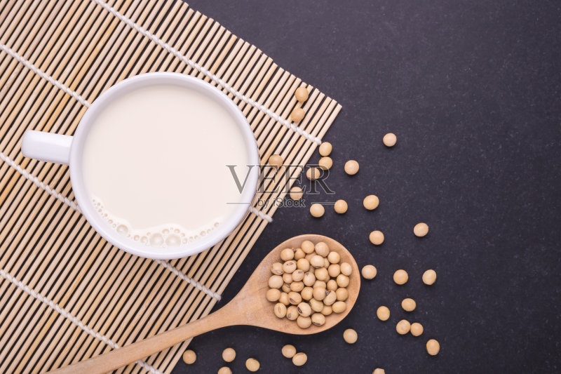 白杯子里的豆浆，黑桌子上的黄豆。俯视图正版图片素材