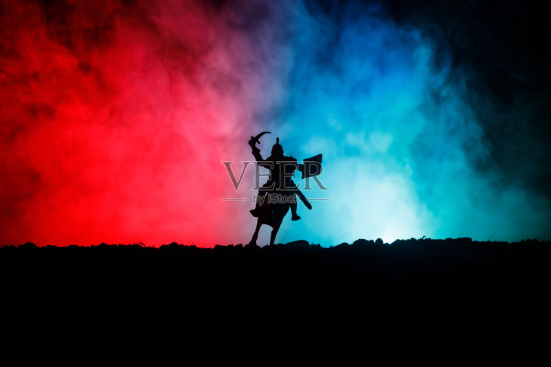 有骑兵和步兵的中世纪战斗场景。剪影的人物作为单独的对象，战斗的战士之间的黑暗色调的雾背景。夜景。正版图片素材