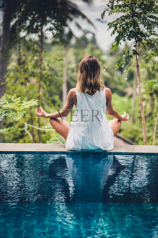 后视图放松的女人锻炼瑜伽在一个无限泳池的边缘。正版图片素材