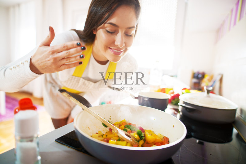 年轻迷人的漂亮女人微笑着，闻着她正在做的新鲜健康的早餐的香味。正版图片素材