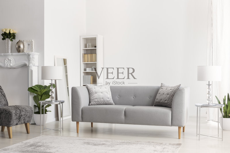 灰色的沙发和灯在银色的桌子在白色的公寓内部与鲜花和扶手椅。真实的照片正版图片素材