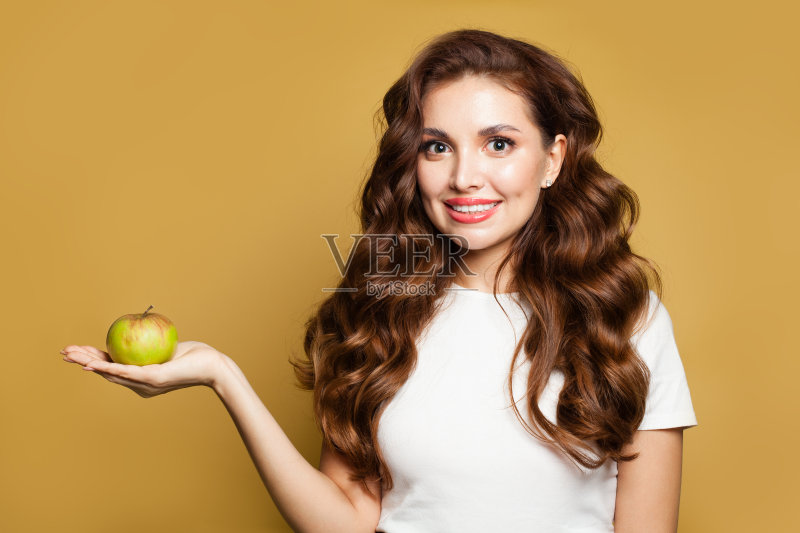 年轻美丽的女人与完美清晰的皮肤保持干燥皱纹的苹果在黄色的背景正版图片素材